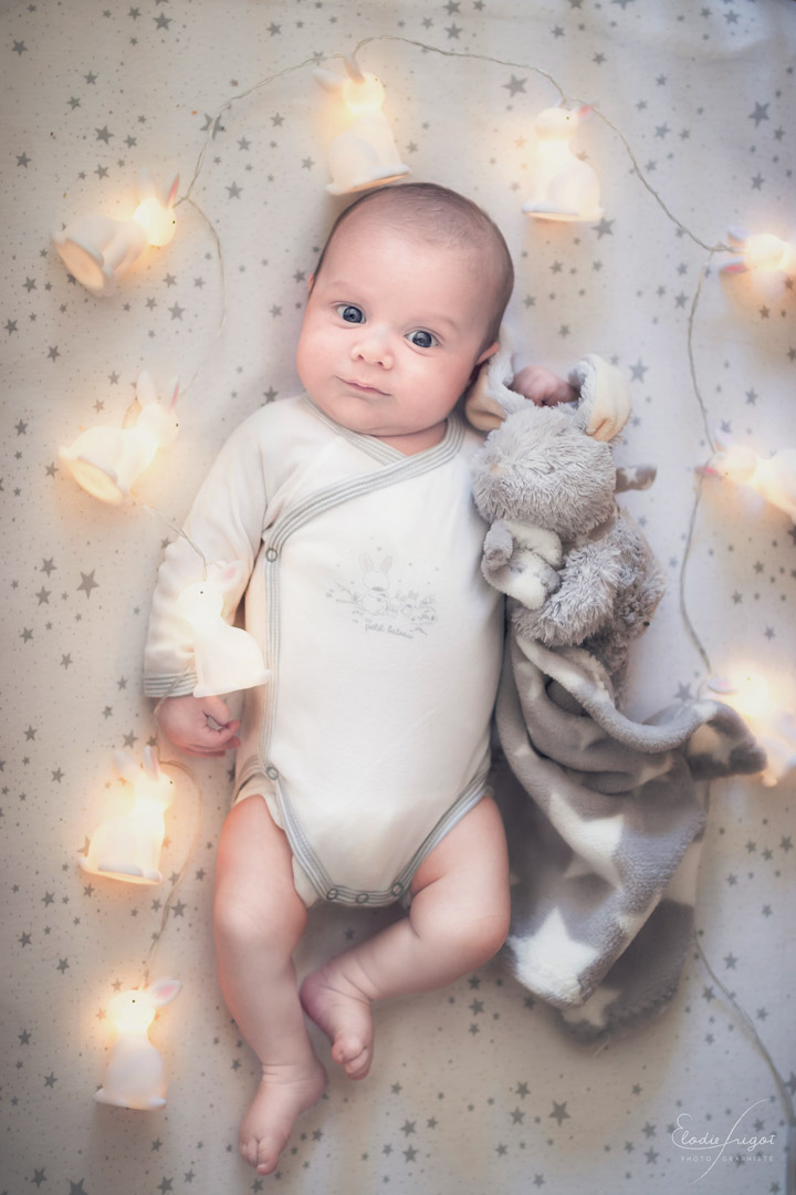 Photo de naissance bébé dans son lit avec doudou et guirlande lumineuse